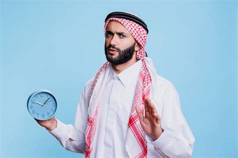 Overslept muslim man dressed in cultural clothes holding retro alarm ...
