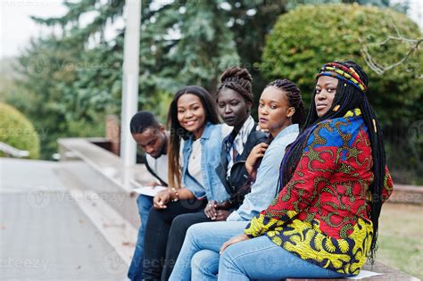 Group of five african college students spending time together on campus at university yard ...