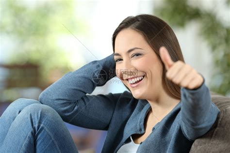 快乐的女人笑手举起拇指坐在沙发上家里的客厅沙发上高清图片下载-正版图片304511002-摄图网