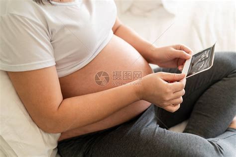孕妇在照顾孩子的同时在家感到快乐年轻的准妈抱着婴儿在怀孕的肚子里产前护理和高清图片下载-正版图片506100255-摄图网