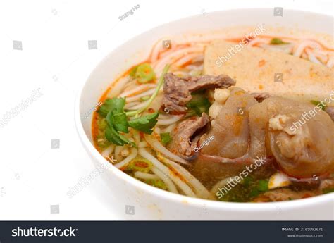 white bowl of beef noodle soup with hardboiled egg halves and sliced green onion on grey countertop