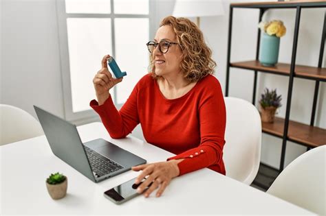 Middle age caucasian asthmatic woman using inhaler sitting on the table ...