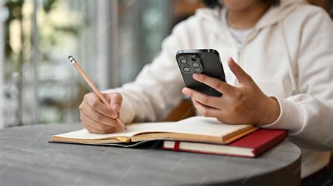 Premium Photo | An Asian female college student using her smartphone while doing her homework at ...