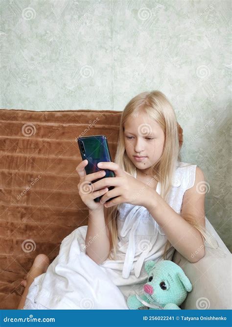 A Little Girl is Sitting on the Couch and Playing on Her Mobile Phone ...