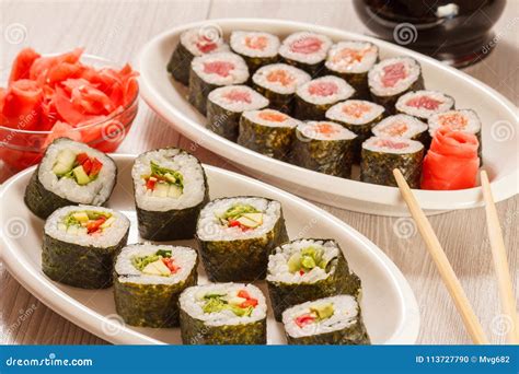 Different Sushi Rolls on Ceramic Plate, Chopsticks, Glass Bottl Stock ...