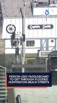 Person uses paddleboard to get through flooded Huntington Beach streets
