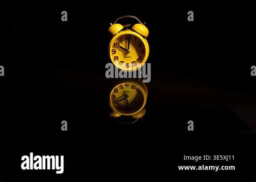 Central timelapse video of a yellow bedside alarm clock showing its reflection on the surface against a black background Stock Video Footage - Alamy