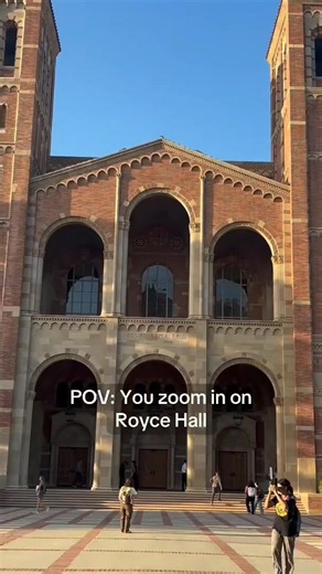 It's all in the details. ? [Video description: A wide shot of Royce Hall?s red-brick facade zooms toward its arched entrances. A montage of close-up shots shows carved stone columns, an owl relief, decorative arches, patterned brickwork, colorful stained-glass windows, engraved lettering above wooden doors, painted ceiling designs, and brick towers. On-screen text reads: ?POV: You zoom in on Royce Hall.?]
