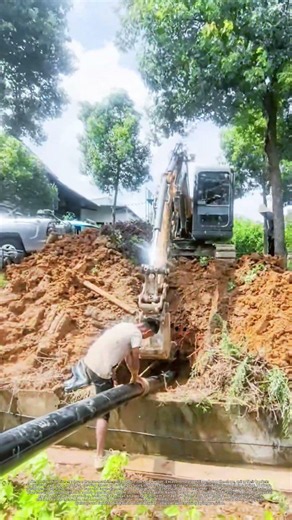 Rural water pipeline construction with excavator digging and worker placing pipes