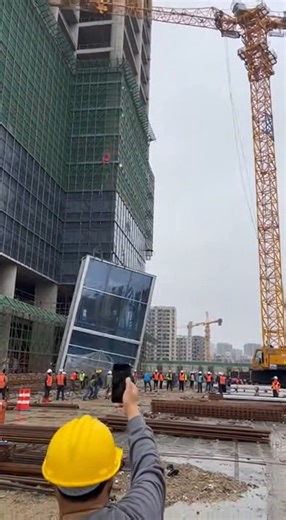 Tower Crane Collapses Under Heavy Load, Workers Flee as Structure Crashes Into Building Urban Construction Site — A catastrophic crane failure was caught on video after a mobile tower crane collapsed while lifting an oversized load at a high-rise construction site. Footage shows the crane fully extended beside a partially completed building when the boom suddenly begins to dip under strain. Within seconds, the crane’s arm buckles. The massive structure twists violently, snapping backward as the 