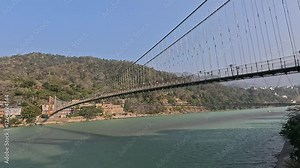 Stunning 4K footage of Ram Jhula spanning the sacred Ganges River in Rishikesh. The serene landscape captures the spiritual essence of this iconic location, surrounded by lush greenery