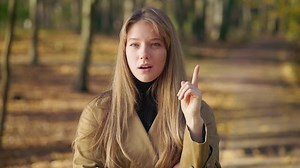 Front view of attractive, young lady wearing elegant clothes, walking in park. Beautiful woman standing squint, looking at camera, remembering. Concept of beauty of nature.