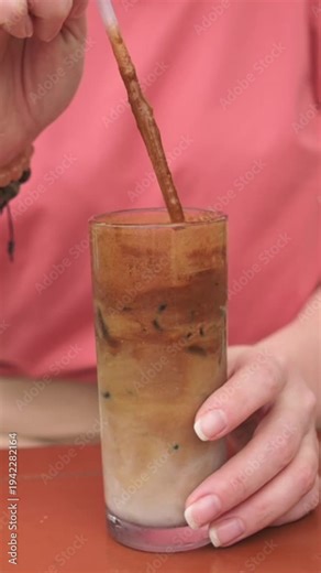 Vertical screen Closeup Caucasian Hand Stirring Iced Latte, Home Barista Mixing Espresso And Milk Over Ice In Tall Glass, Visible Layered Crema And Milk, Creamy Swirl Motion With Straw, Pink