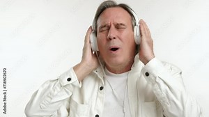An ecstatic senior man fully immerses in the rhythm, wearing headphones and singing out loud with a passionate expression, isolated on a white background. Camera 8K RAW. Stock Video