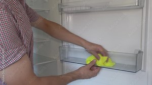 a man's hand washes the refrigerator, cleaning the refrigerator in the kitchen, wiping the open refrigerator with a rag
