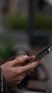 Closeup vertical cropped shot of unrecognizable businesswoman using smartphone, scrolling screen in city setting, browsing internet and texting, on blurred urban background, slow motion