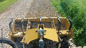Box scrapper leveling a new graveled driveway and gravel that is in the box is distributed along the driveway; concepts of blue collar work, hydraulics, new construction and country life
