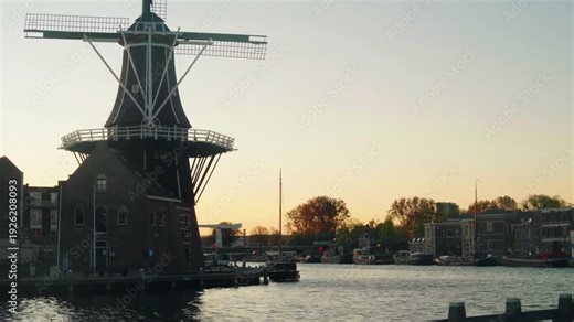 Historic Dutch windmill stands tall by the canal at sunset with boats and buildings in the background