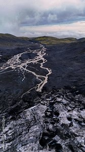Volcanic ground of black color crossed by the lines of the narrow rivers. Amazing scenery of Iceland scenery from top. Vertical video.