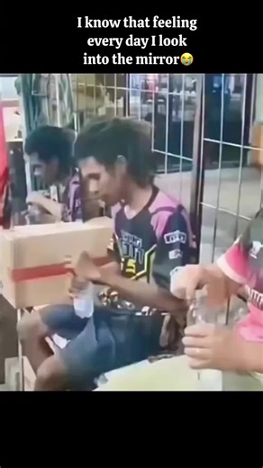 Bro forget his own face 😂😂 In this video, a man with long, dark hair is seen sitting and drinking water from a plastic bottle. As he takes a sip, he suddenly spits the water out in a large spray, seemingly surprised or reacting to something off-camera. Another man sitting next to him, wearing a pink and black jersey, watches this happen and begins to laugh heartily. The man who spit out the water also joins in the laughter, leaning forward as they both find the situation hilarious. The backgro