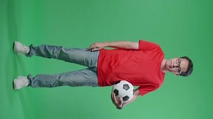 Full Body Of Asian Man With A Ball Showing Thumbs Down Gesture For Making Fun Of The Losers While Cheering Soccer On Green Screen Background
