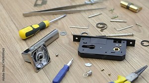 The disassembled internal door lock lies on the table. Screwdriver, spring, hexagons, tweezers, lock core and door handle. Door lock repair.
