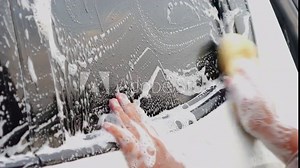Man's hand uses a sponge to wipe the car glass. Take care and wash your car with wash liquid. Clean the car by yourself