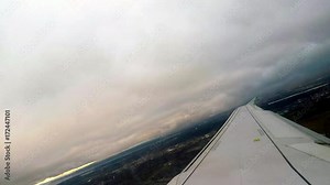 Canted angle shot over wing of airplane as it penetrates the clouds over Montreal, Canada, as the sun rises on a cloudy day.
