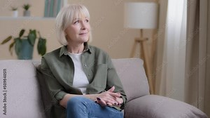 Happy dreaming inspired thoughtful elderly old Caucasian 60s woman looking away in window sit on sofa alone think, pensive senior lady middle-aged grandma relaxing contemplate dreams at home couch