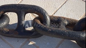 Iron chain - series of metal stud links. Heavy steel anchor bond, black with some rust, on white stone tiles.