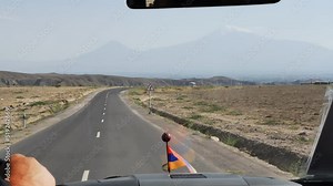 Looking into the windshield of a car driving along the highway towards the high snowy mountains. Close to Mount Ararat or Masis. Armenian highway in the Ararat valley