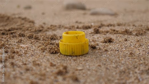 Garbage on the sand of an ocean beach in France, a yellow bottle cap
