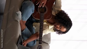 Vertical video. Online music school. Guitar lesson. Remote learning. Woman guitarist practicing string instrument chords virtual class on laptop sitting home couch.