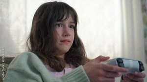 11 years old child holding gaming console and playing on a sofa. Portrait of pre-teenage girl with video game remote control playing a video game, holding joystick, smiling. Children's Leisure And Stock Video