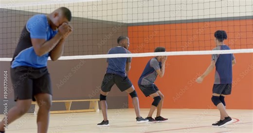 Diverse male volleyball team reacting to serve with net block then regrouping on court for huddle