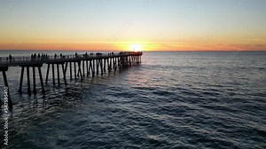 Hermosa beach pier at sunset, with people walking and watching the sun go down