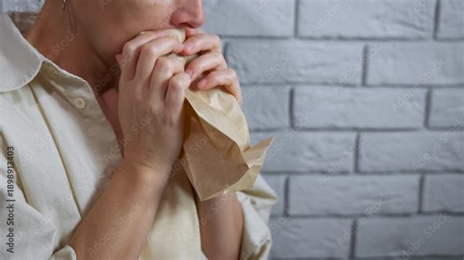 Stressed woman breathing into paper bag for panic attack. Distressed woman suffering from anxiety and hyperventilating, breathing into a paper bag to calm down her panic attack