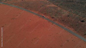 Arid Red Desert With A White Vehicle Park In Asphalt Road During Summertime In Northern Territory, Australia. - Aerial Descending Shot