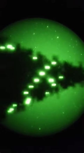 DAY 65 — Lens Drift Over Unidentified Tree Lights Surveillance log, December 24 – long‑range night‑vision lens locks onto a tree‑line structure showing multiple independent light sources. Lights remain suspended with no visible cables, wind movement or ground activity. No registered aircraft or drones in the area at the time of capture. Signal density increases toward the upper branches before fading without a trace. Source of illumination and power remains unidentified. What do you think this i