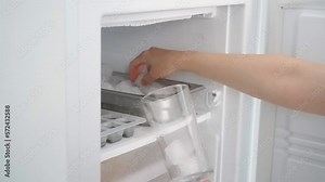 The girl takes ice cubes from the freezer or puts them in a glass for a cold drink.
