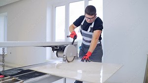 Tiler cutting tile on wet saw machine. The master cuts the tiles. Circular saw with bathtub for liquid. Tile Production Workshop. person works stone and large ceramic tile. Professional equipment