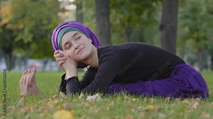 Beautiful young islamic woman wears hijab sitting on grass in park outdoors bending over in body belly stretching stretch doing yoga exercise physical training workout resting relaxing smiling