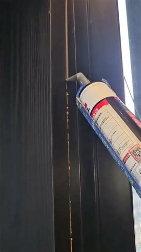 sealing a dark window frame joint precisely using a professional manual caulking gun in indoor area