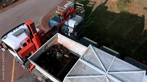 Refuse truck is collecting recycled glass from containers by the roadside, lifting up and unloading them in the back of the truck, glass recycling concept.