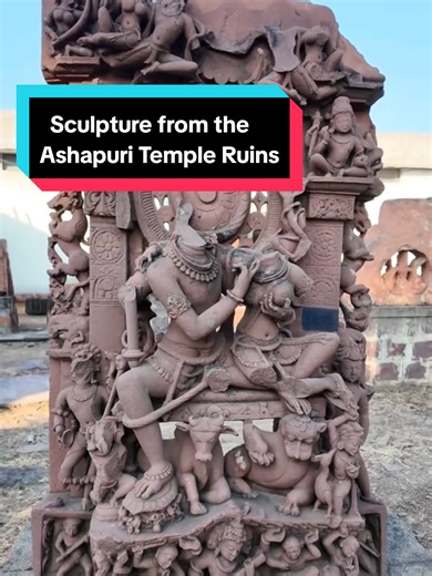 Sculpture from the Ashapuri Temple Ruins This elaborate stone sculpture once formed part of the decorative program of the medieval Ashapuri temple complex in Madhya Pradesh, India. The composition is built as a dense vertical shrine-like structure, filled with divine figures, attendants, animals, and mythological beings carved in layered registers. At the centre sits a divine couple beneath a richly ornamented arch, framed by a large circular halo or wheel-like motif behind them. The figures are