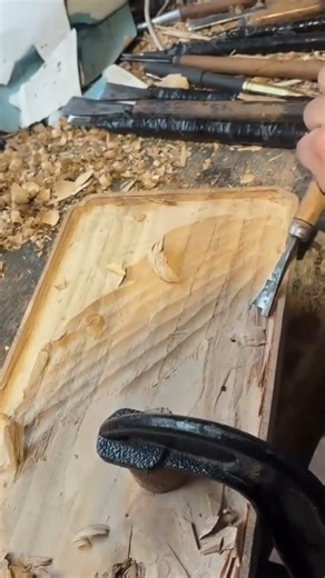 carving a decorative wavy pattern onto a flat wooden board using a sharp metal wood chisel tool