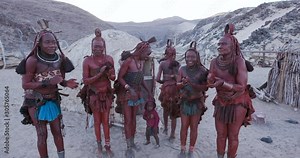 4K view of Himba woman in traditional dress dancing and singing outside their clay hut, Namibia