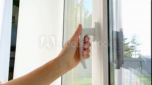 The hand holds the handle of a plastic double-glazed window, closing and opening the window with a rotary mechanism, the position of the handle for ventilation, micro-ventilation