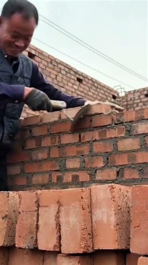 building a tall red brick wall by layering bricks and cement mortar carefully on a construction site