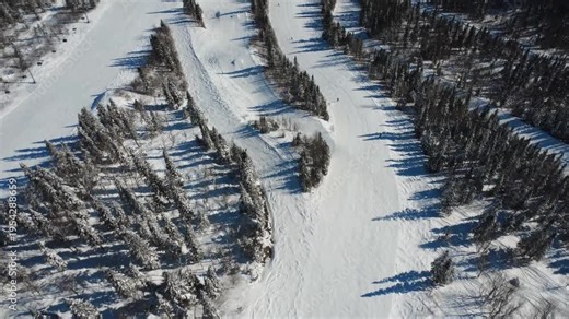 Top-down drone footage of a group of alpine skiers carving down a groomed slope toward the base of Val d'Irene resort in Sainte-Irene, Quebec. Bright winter scenery and mountain lifestyle.